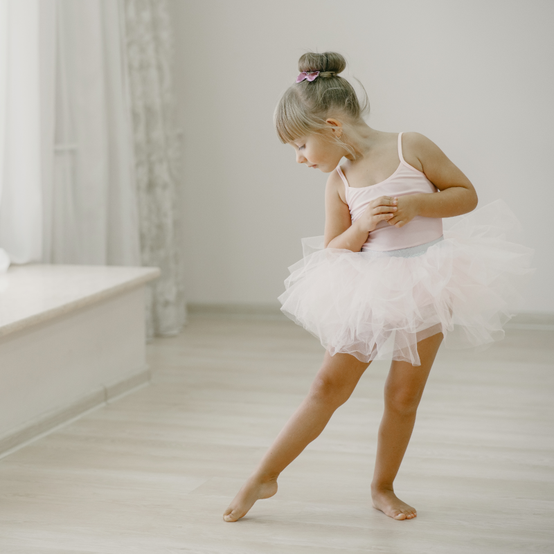 Una niña de 6 años vestida de blanco con tutu y maiot haciendo ballet descalza