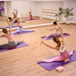 chicas realizando clase de estiramientos sentadas sobre un bloque de yoga y estirando con un cinturón.
