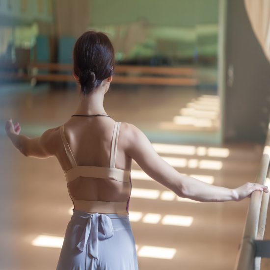 Bailarina de ballet clásico de espaldas con una mano sobre la barra preparando un ejercicio