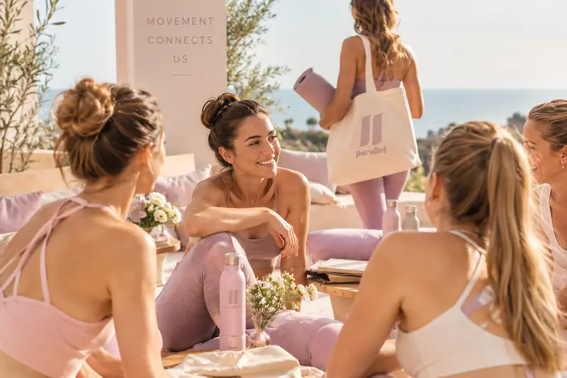 unas chicas hablando en un evento de bienestar. Van vestidas de rosa y llevan bolsas de parallel