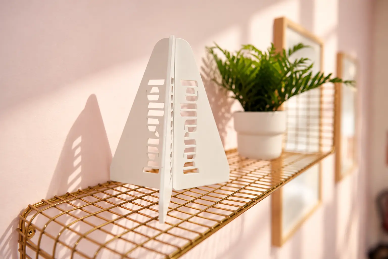 estante dorado con una figura de un pata de una barra de ballet donde se puede leer "parallel". Al lado una bonita planta con una maceta blanca.